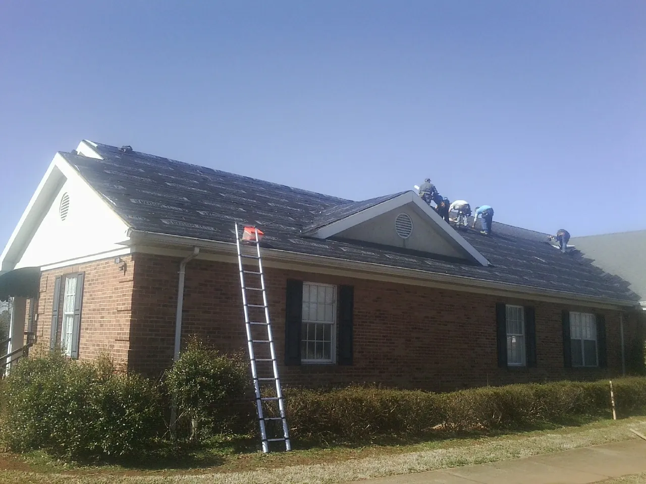 Crew tearing shingles off a brick ranch roof with a ladder set — Metal Roof Repair work by our crew in Millington