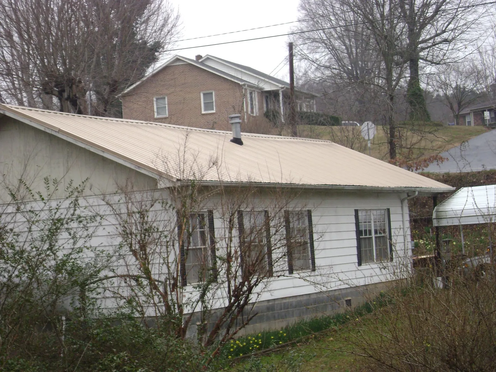 Tan metal roof on a white sided house set into a hillside — Commercial Roofing by Roofing Brothers in Millington